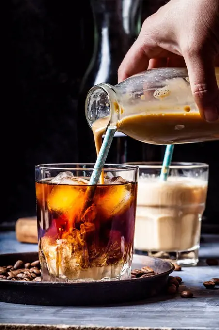 Hand pouring homemade vanilla flavoured coffee creamer into a glas with iced coffee