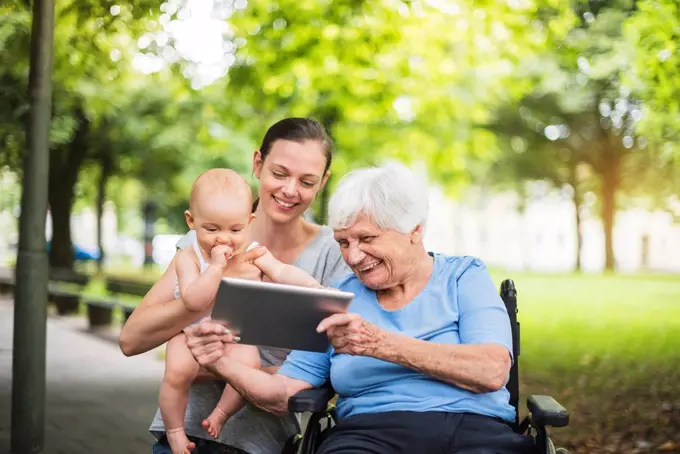 Grandmother, daughter and granddaughter having fun with tablet in a park