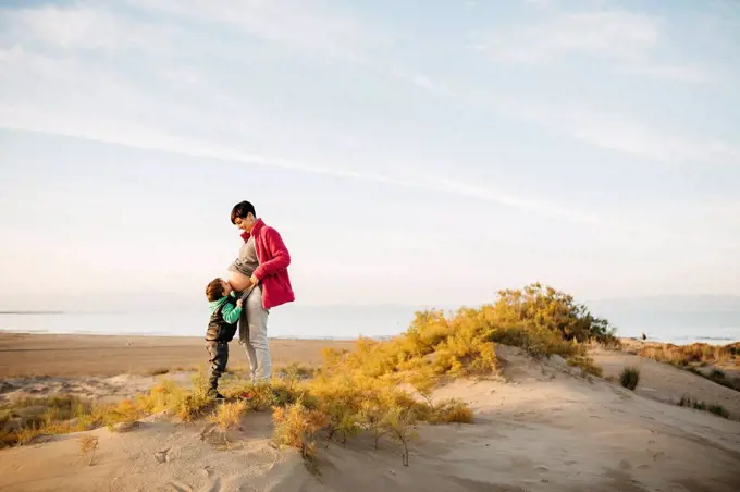 Son kissing pregnant mother's belly on the beach in winter