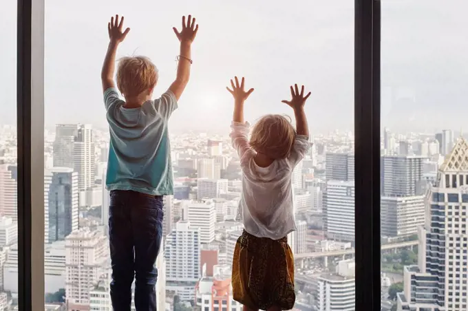 Thailand, Bangkok, boy and little girl looking through window at cityscape