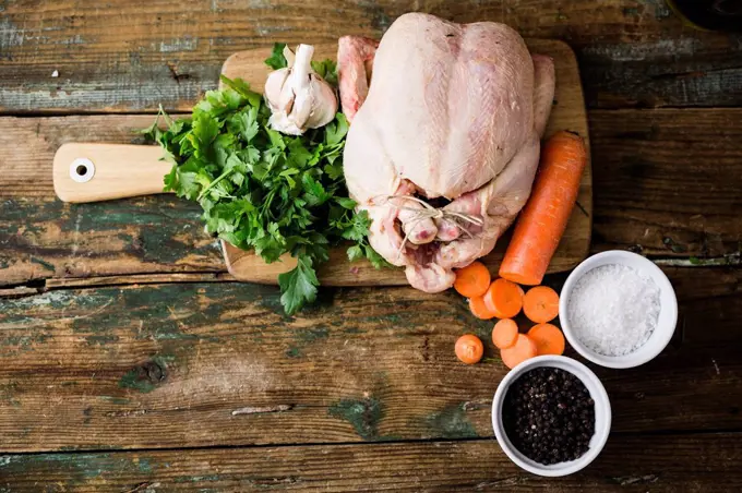 Raw chicken with carrots, parsley, garlic, pepper and salt on a chopping board