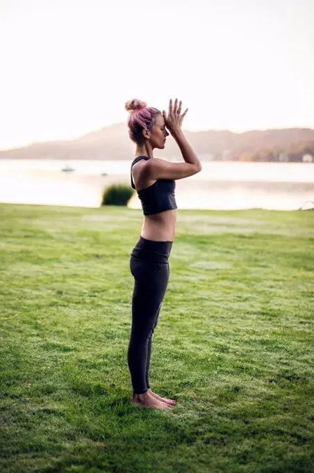 Woman in sportswear standing on a meadow meditating at a lake