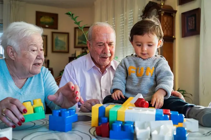 Great-grandparents and baby girl playing together with plastic building bricks at home