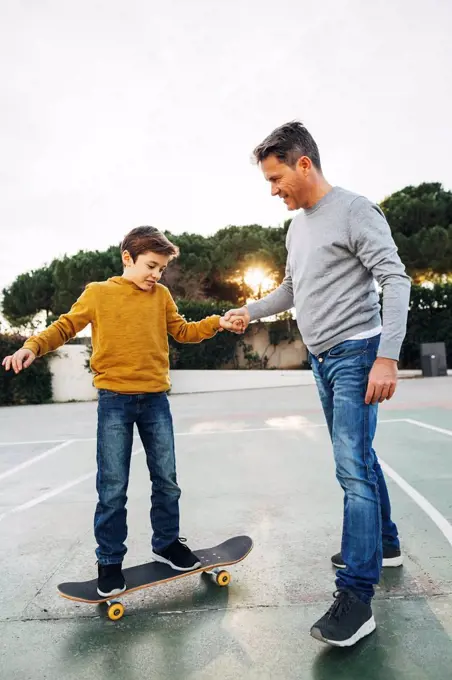 Father assisting son riding skateboard