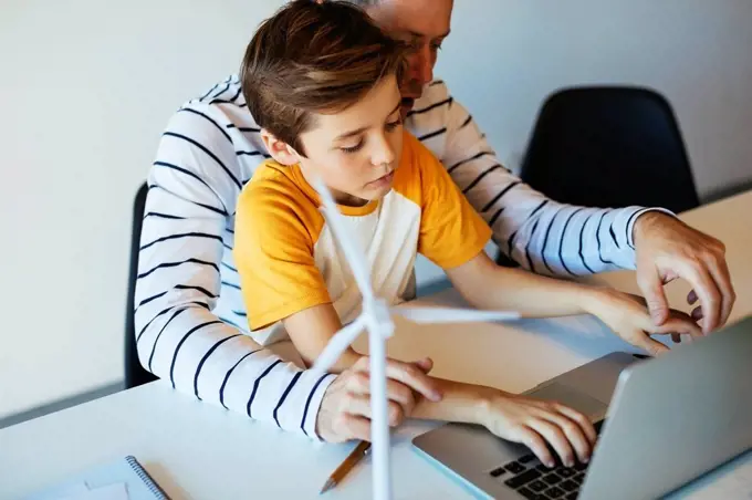 Father and son using laptop next to wind turbine model