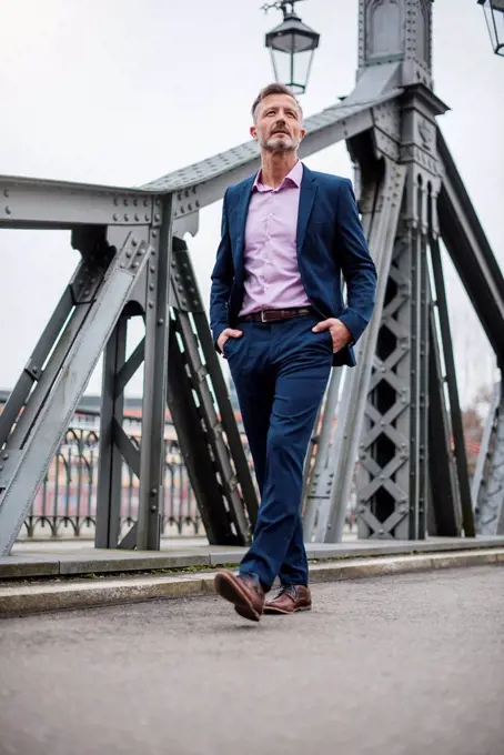 Stylish mature businessman wearing blue suit walking on bridge