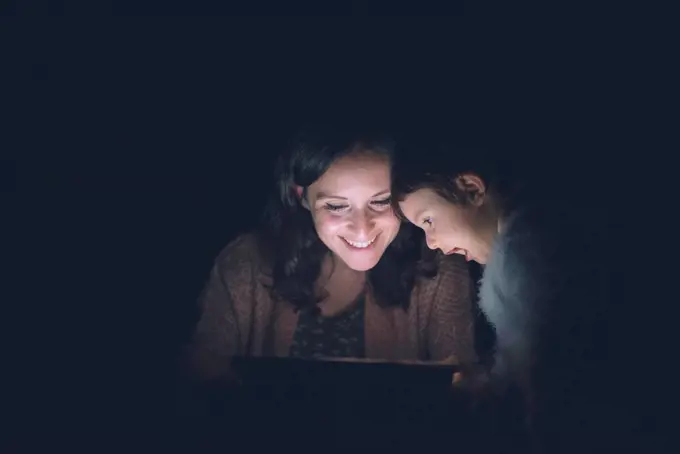 Mother and daughter using digital tablet at home in the dark