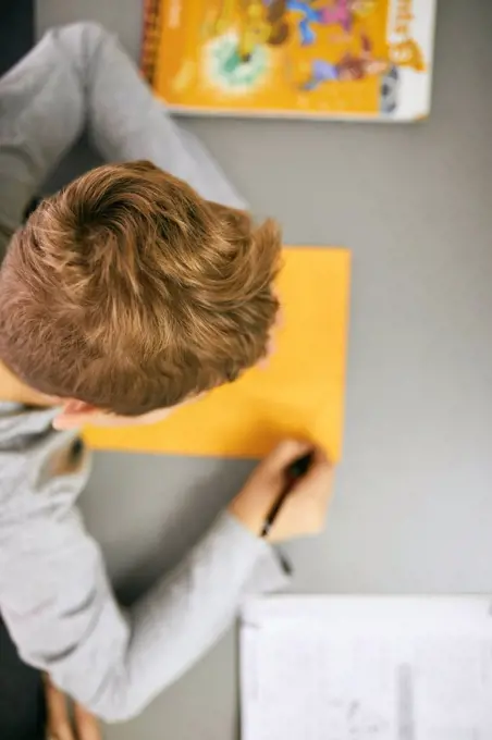 Schoolboy writing on desk in class