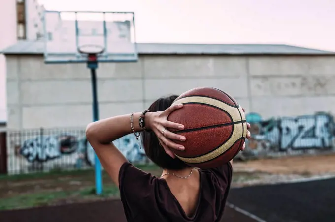 Rear view of young woman holding basketball on outdoor court