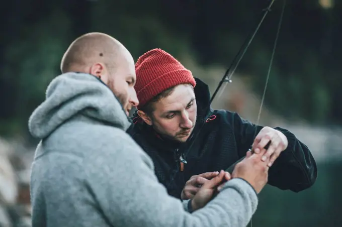 Young man helping friend with fishing rod