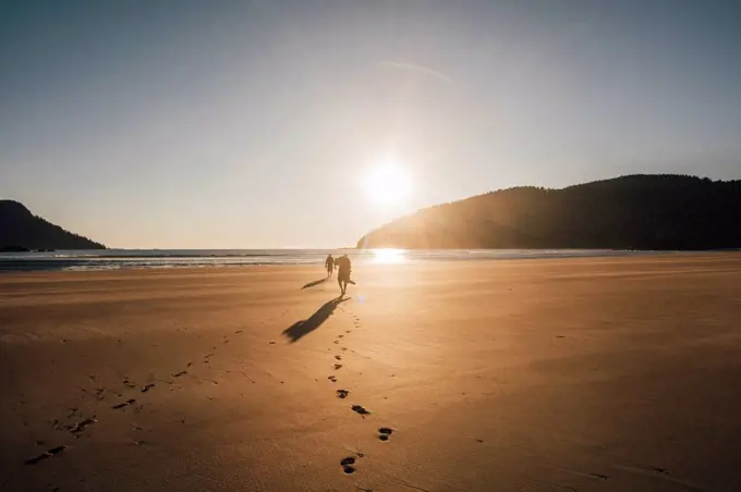 Canada, British Columbia, Vancouver Island, two men walking on beach at San Josef Bay at sunset