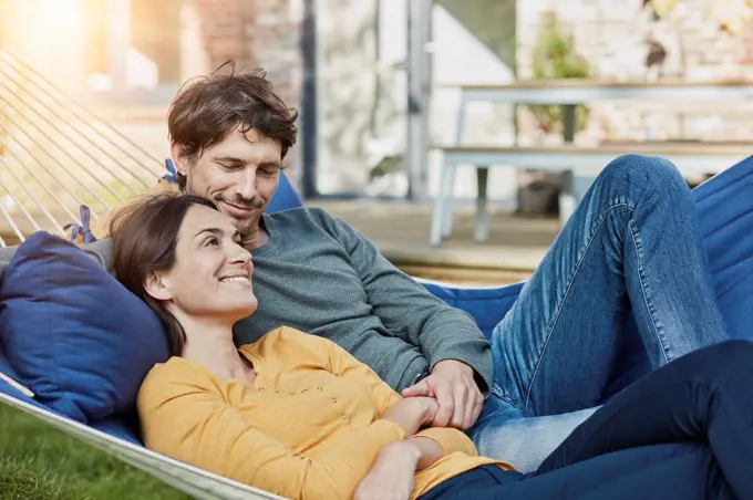 Smiling couple lying in hammock in garden of their home