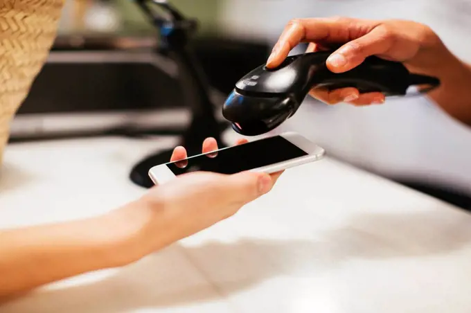 Close-up of customer paying cashless with smartphone at counter of a store