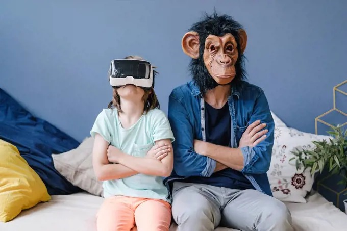 Father wearing monkey mask sitting next to son wearing VR glasses at home