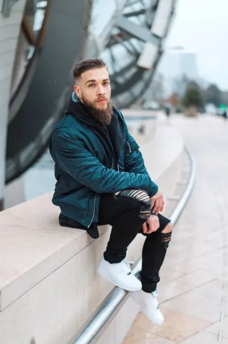 France, Paris, portrait of bearded young man sitting on a wall