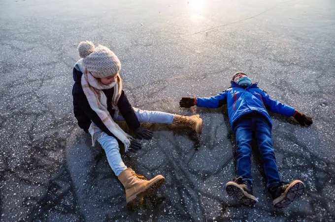 Germany, Brandenburg, Lake Straussee, two kids sitting and lying down on frozen lake