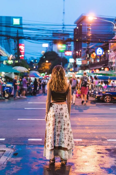 Thailand, Bangkok, young woman in the city standing on the street at night