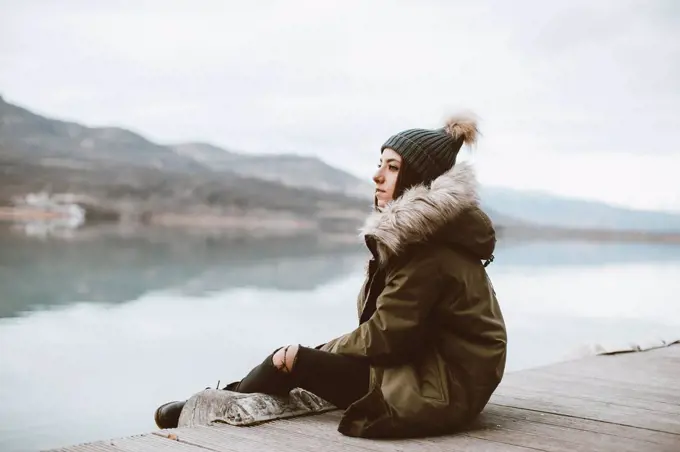 Pensive young woman sitting on jetty looking at distance