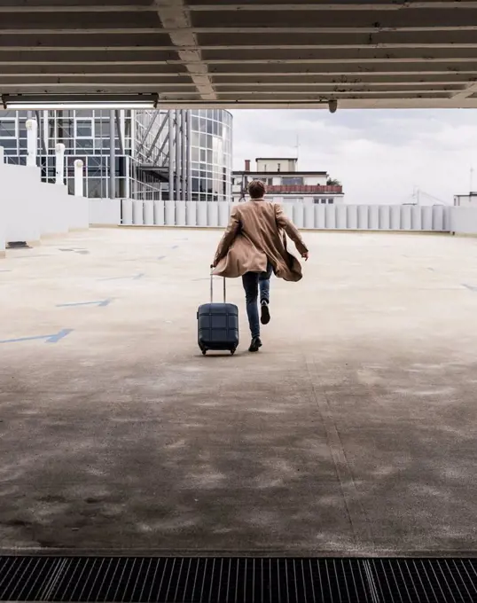 Businessman with rolling suitcase in a hurry at parking garage