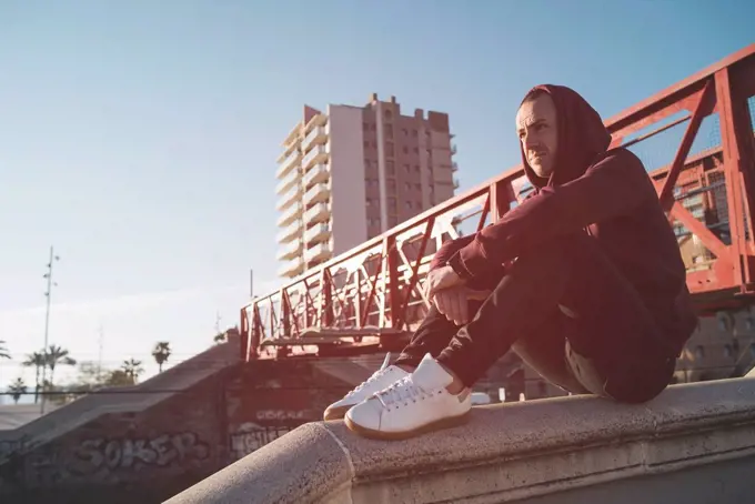 Man with hoodie sweater sitting on wall