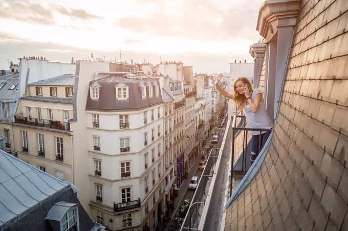 France, Paris, waving woman on the phone standing on balcony looking down