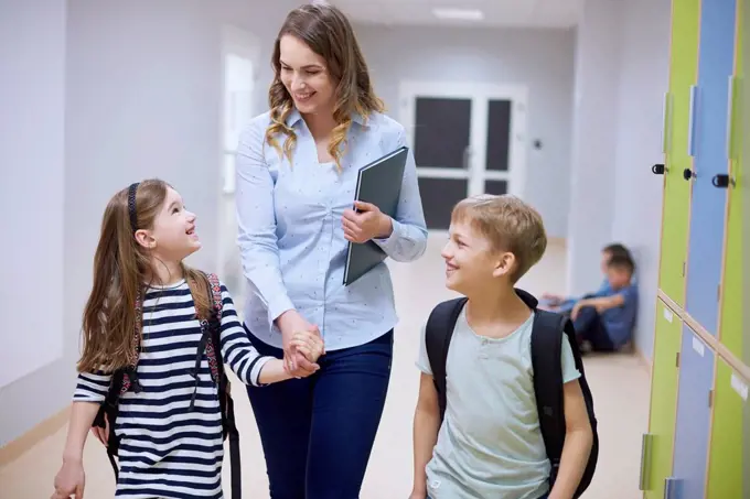 Smiling pupils and teacher walking hand in hand on corridor in school