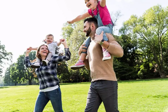 Happy parents carrying children on shoulders in a park