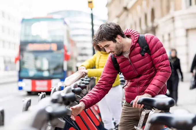 UK, London, young man renting bicycle from bike share stand in city