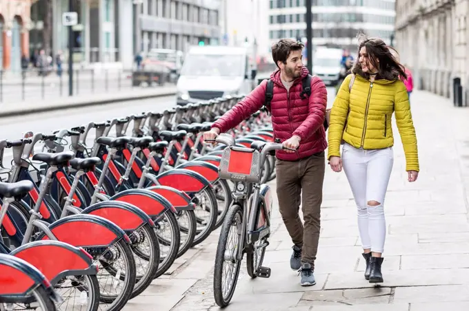 UK, London, young couple with bicycle from bike share stand walking in city