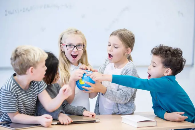 Happy pupils holding globe together in class