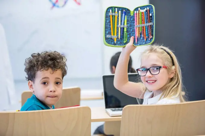 Portrait of schoolboy and schoolgirl with laptop and pencil case in class