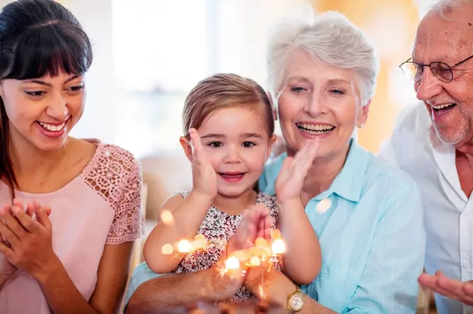 Little girl lwatching sparklers on a birthday cake, sitting on grandmother's lap