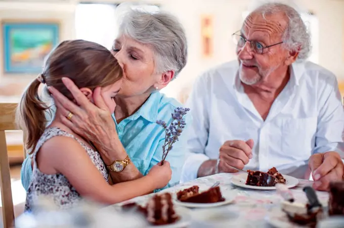 Grandparents celebrating a birthday with their granddaughter, eating chocolate cake