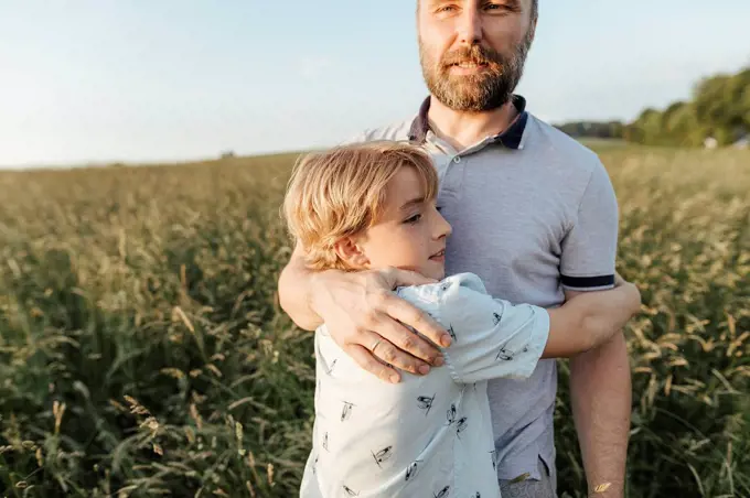 Father and son standing on a meadow hugging each other