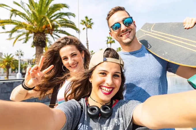 Selfie of three happy friends with skateboard