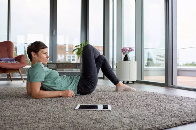 Woman lying on the floor at home with tablet looking out of balcony door