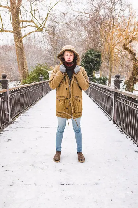 Young man standing on footbridge in a park on a snowy day