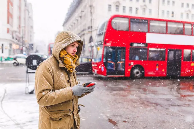 UK, London, young man with cell phone standing at roadside looking at distance