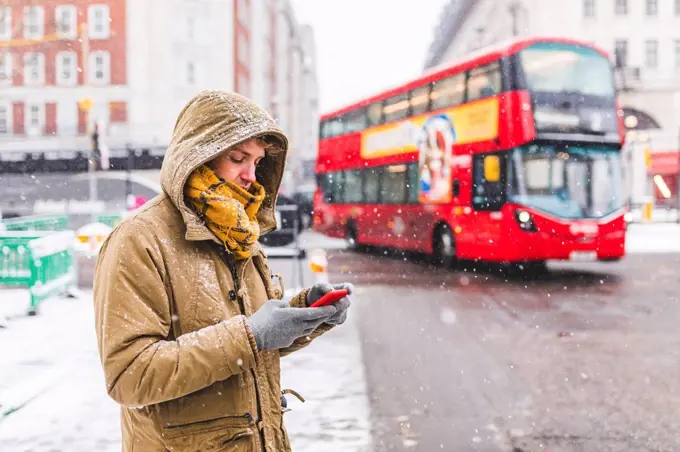 UK, London, young man standing next to the road in the city looking at cell phone