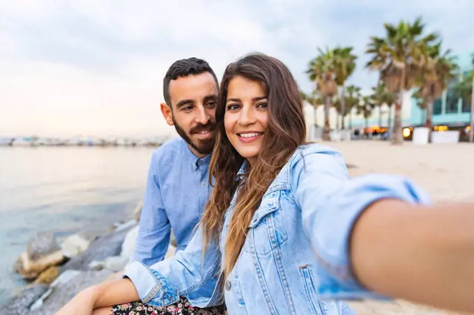 Spain, Barcelona, smiling couple taking a selfie at the seaside