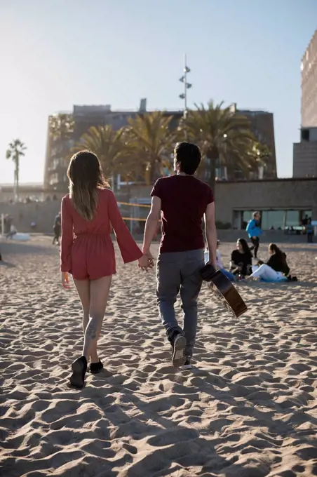 Spain, Barcelona, couple with a guitar walking on the beach