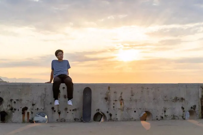 Young Chinese man sitting on wall at sunrise