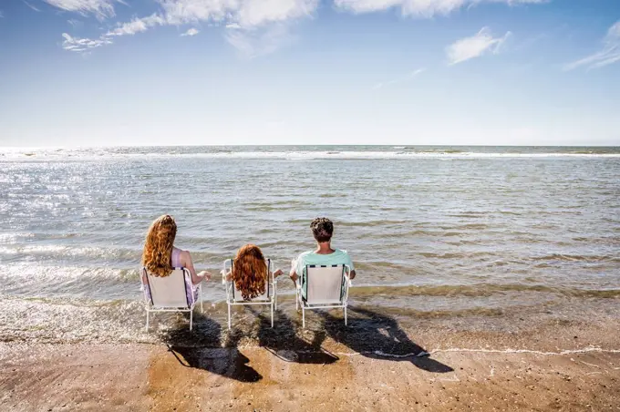 Netherlands, Zandvoort, family sitting on chairs in the sea