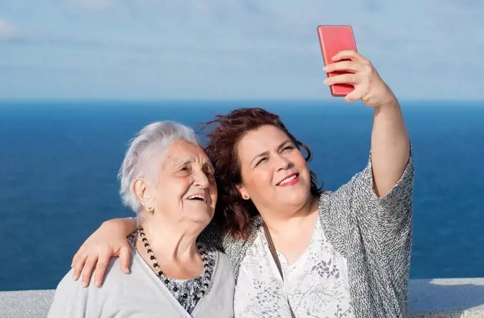 Grandmother and granddaughter taking a selfie in front of the sea