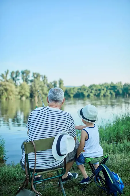 Back view of grandfather and grandson fishing togetehr at lakeshore