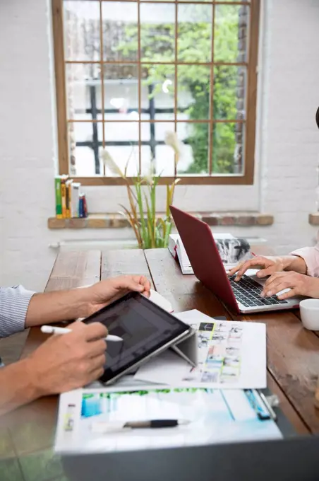 Mature couple working from their home office, using laptop and digital tablet