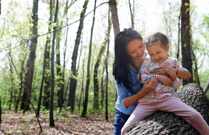 Mother and daughter in park, sitting on tree trunk