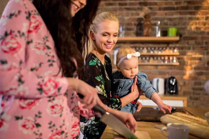 Female friends with baby girl preparing dinner together