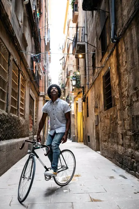 Spain, Barcelona, man standing with racing cycle in an alley looking up