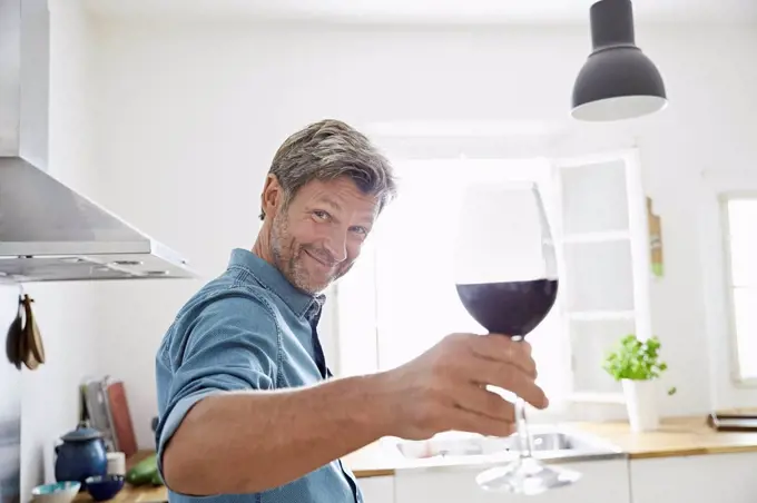 Man in kitchen toasting with glass of red wine